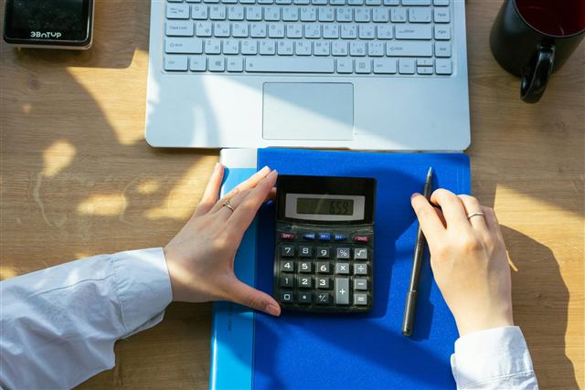 Mãos usando calculadora sobre pasta e notebook em mesa de trabalho