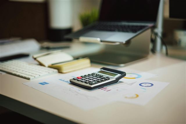 Calculadora sobre relatórios em mesa de trabalho com notebook ao fundo