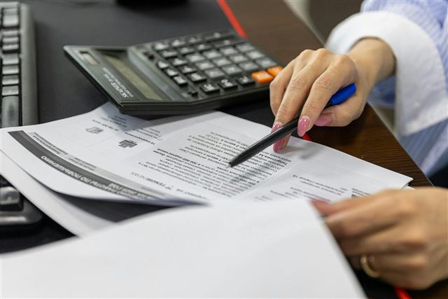 Mãos revisando documento com calculadora e caneta em mesa de trabalho